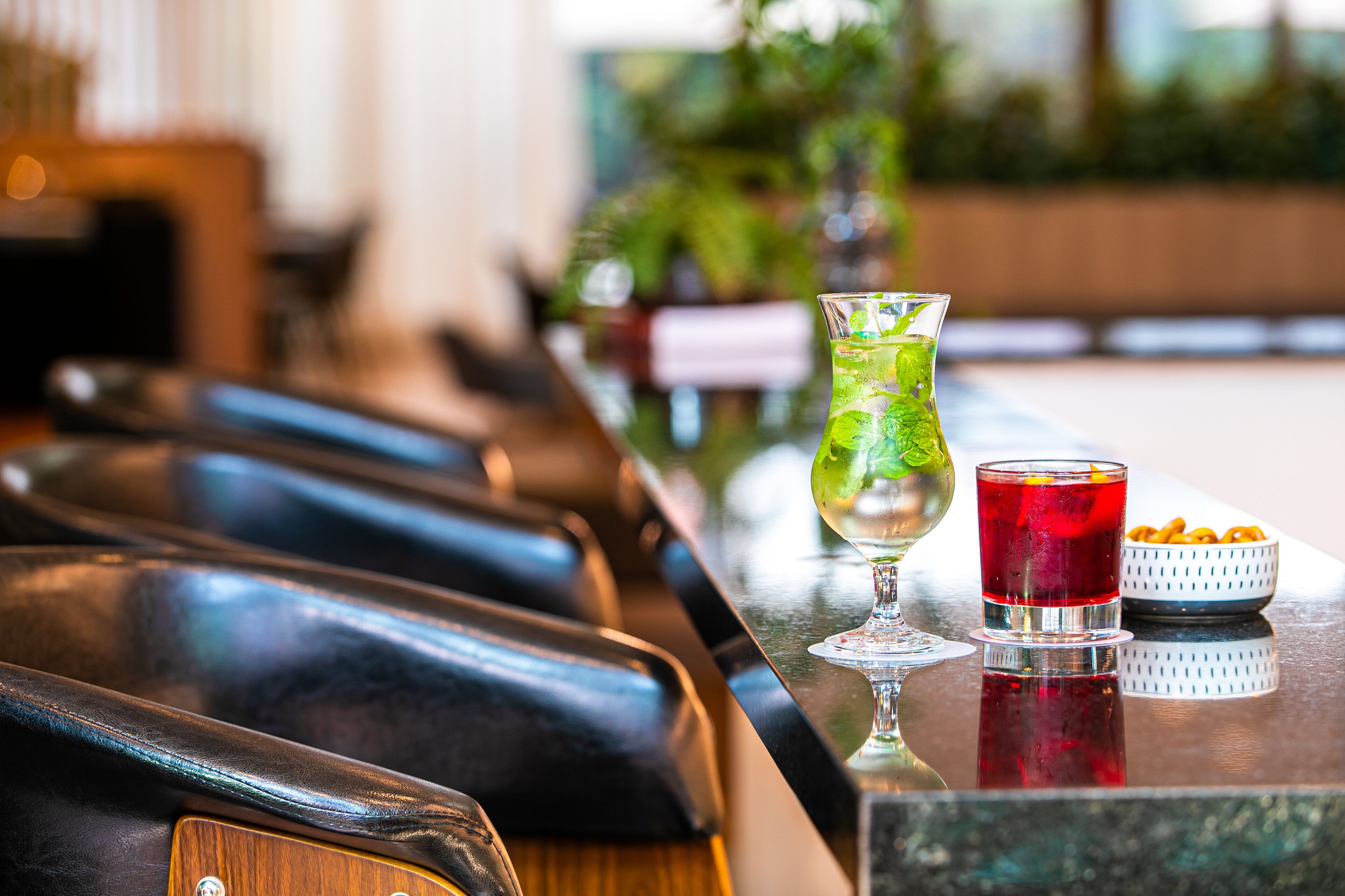 A bar area with a leather bar counter, a glass with a green drink, and a red drink in a shot glass.