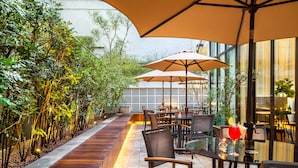 Un patio al aire libre con asientos de madera, mesas y sombrillas.