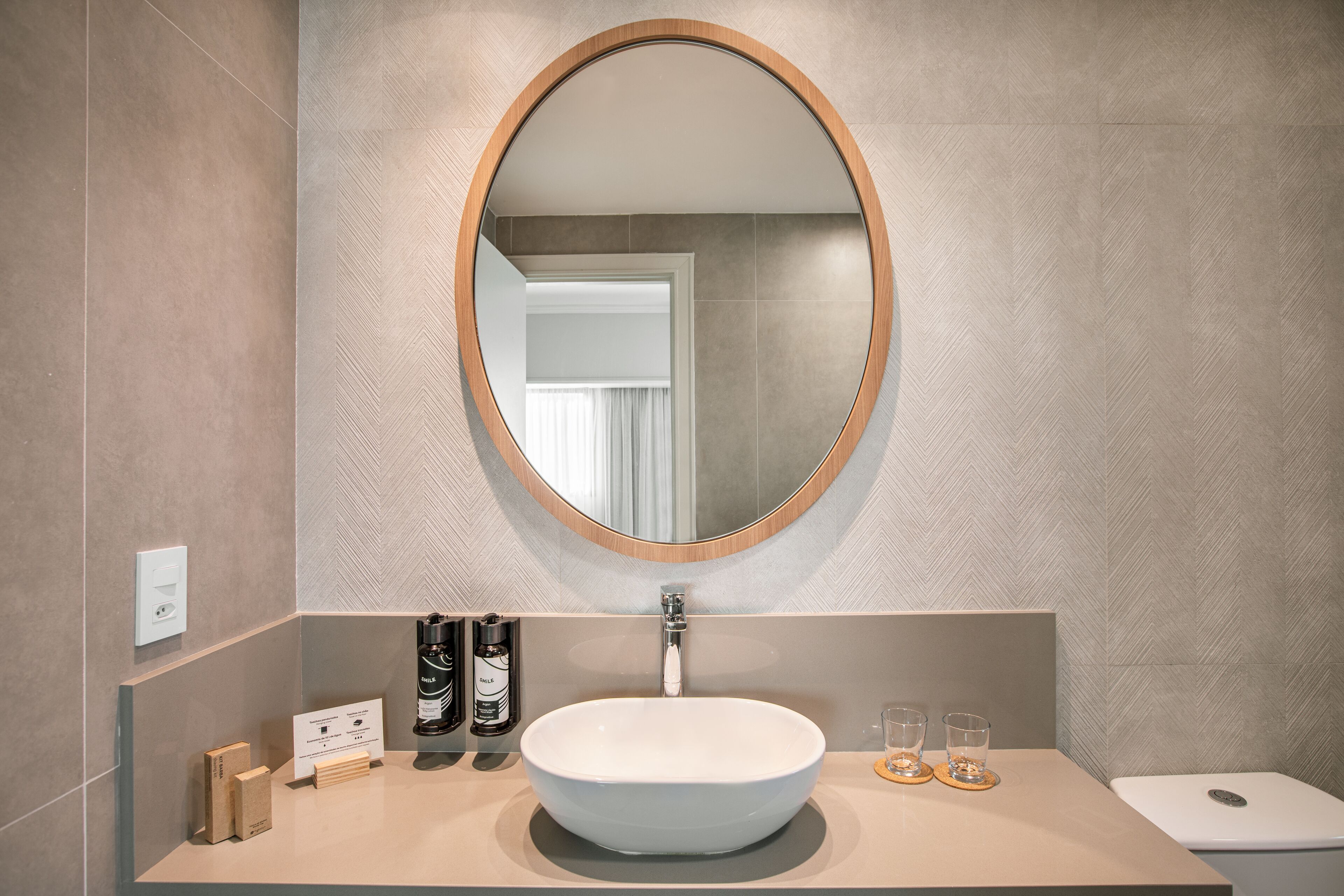 A modern bathroom with a large oval mirror, a white sink, and a toilet.
