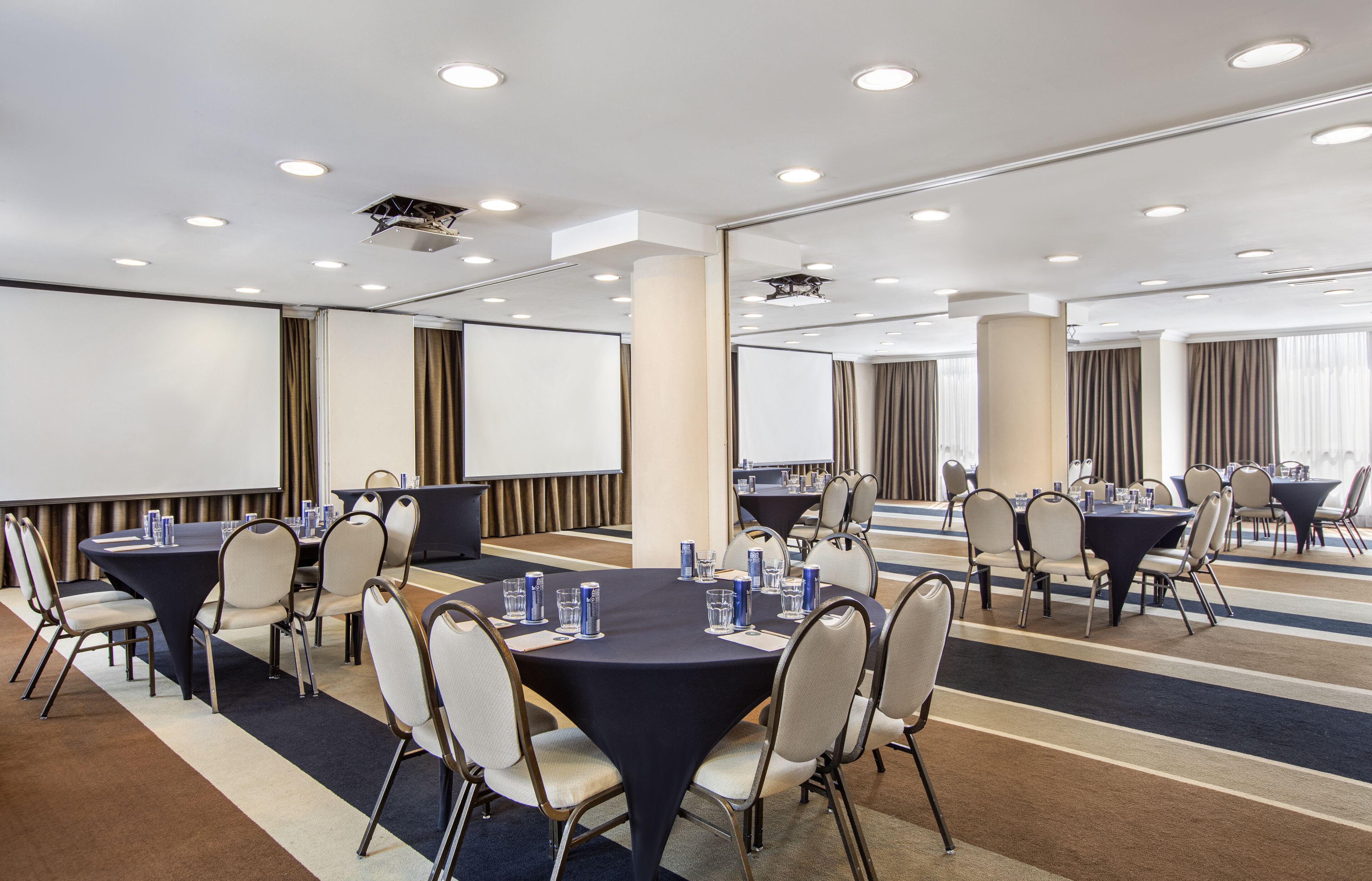 Un salón de conferencias con mesas redondas, sillas y una pantalla para proyector.