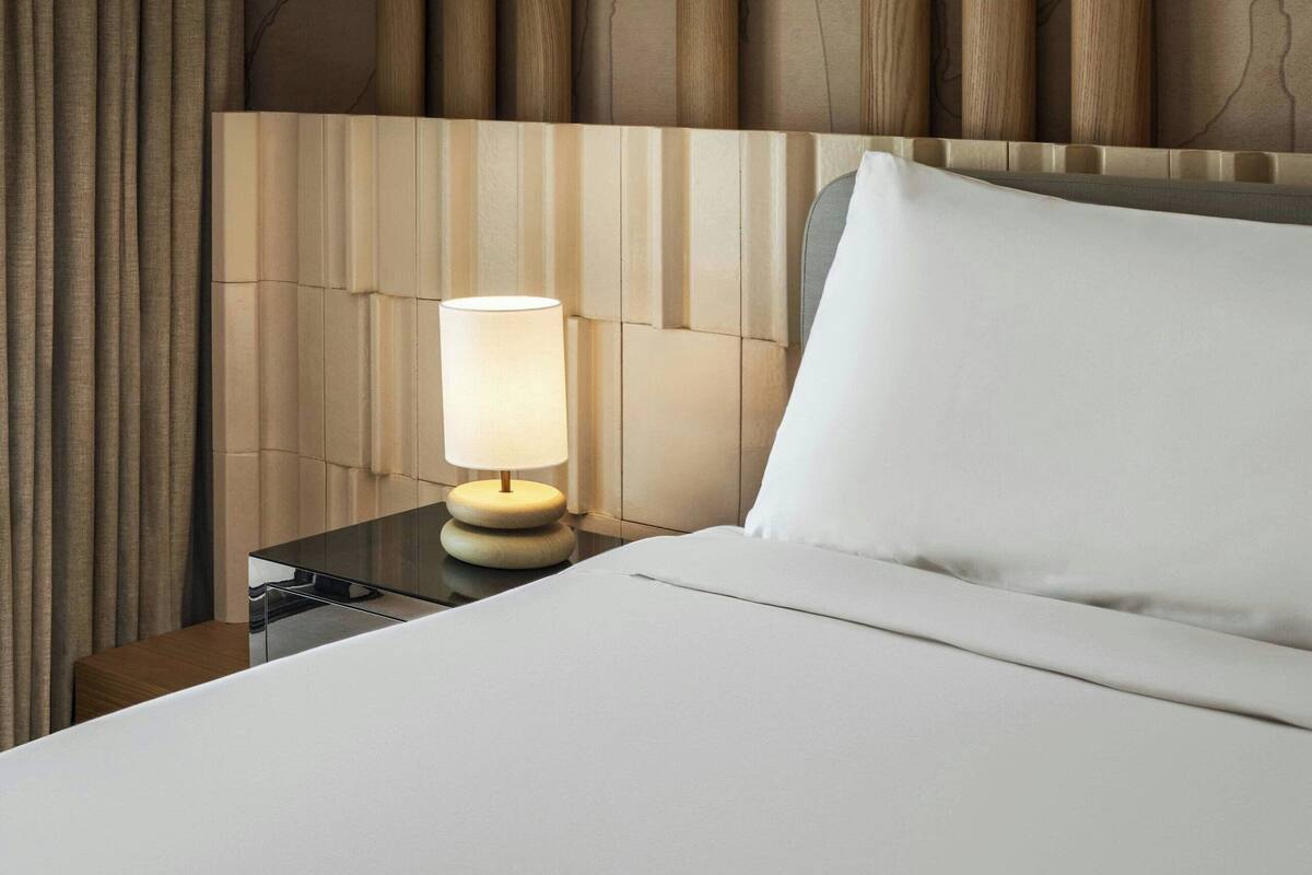 A hotel room with a bed, a nightstand with a lamp, and a headboard with vertical wooden panels.