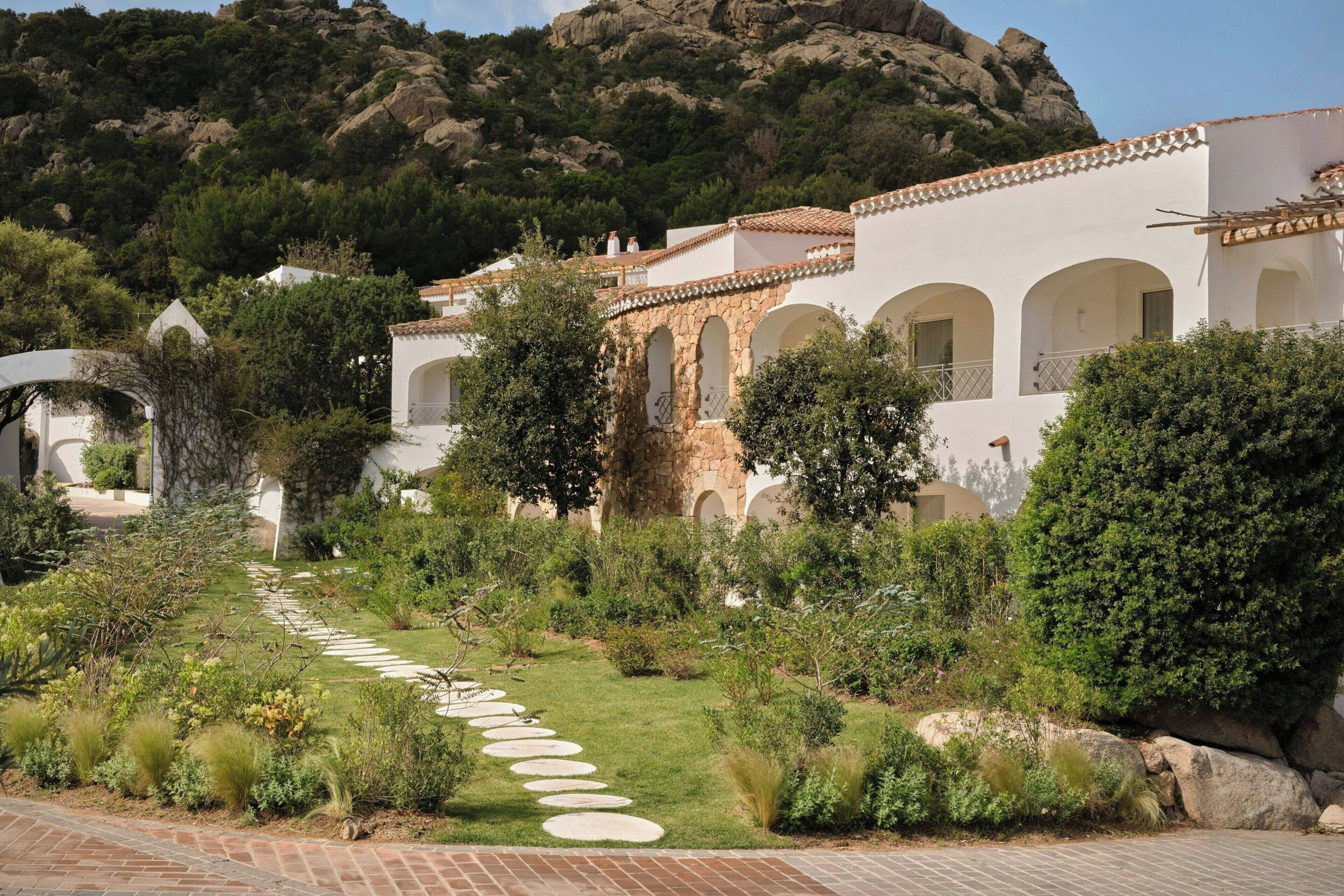 A white building with arches, a stone pathway, and greenery.