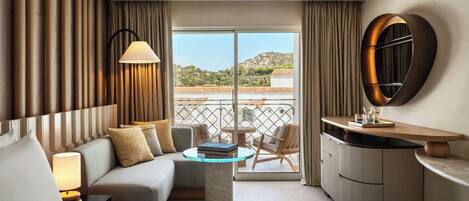 A hotel room with a bed, a sofa, a small table, a lamp, a mirror, and a view of the outside.