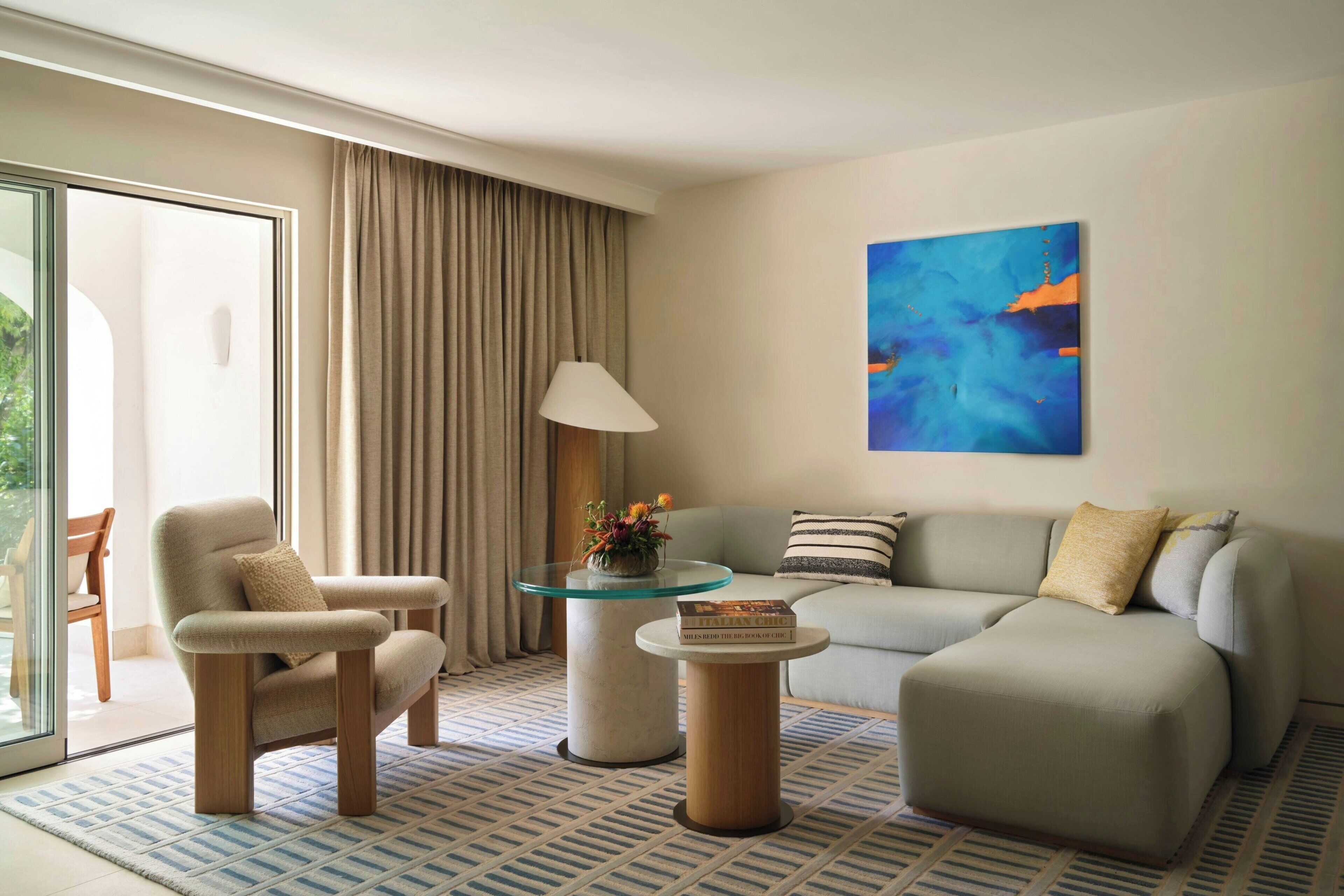 A modern living room with a sofa, armchair, glass coffee table, and a lamp.