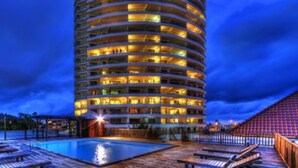 A multi-story hotel with a pool area, including sun loungers and a wooden deck.