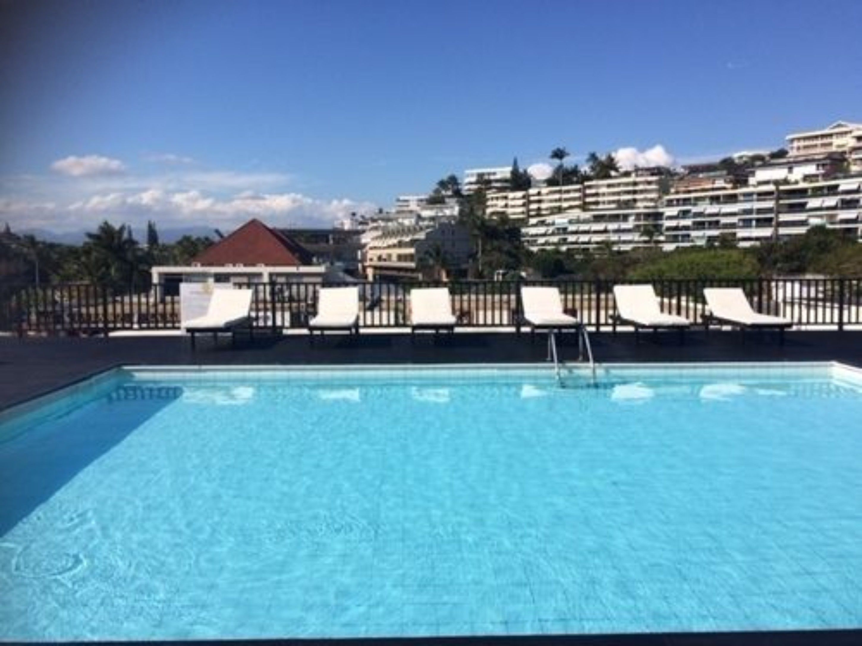 A swimming pool with white lounge chairs and a view of a multi-story building in the background.