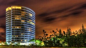 A modern, multi-story hotel with a curved facade, illuminated windows, and a well-lit exterior.