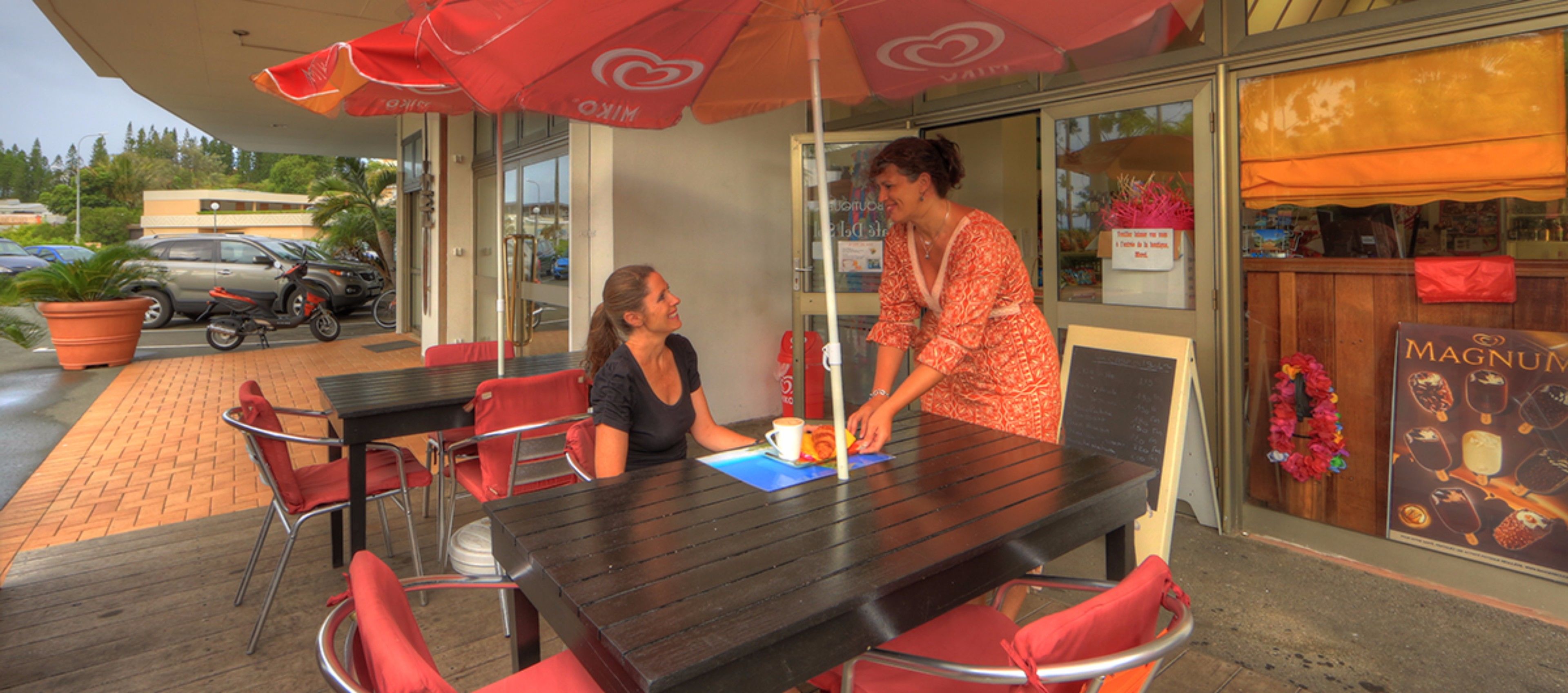 An outdoor seating area with tables and chairs, a menu board, and a storefront with a sign.