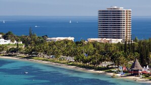 A coastal hotel with a beachfront view, a tall building in the background, and a clear blue sea.