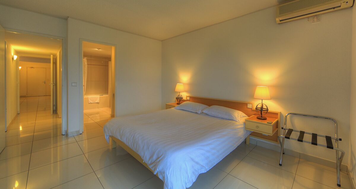 Habitación de hotel con cama, lámparas de noche, una silla de ruedas y zona de ducha.