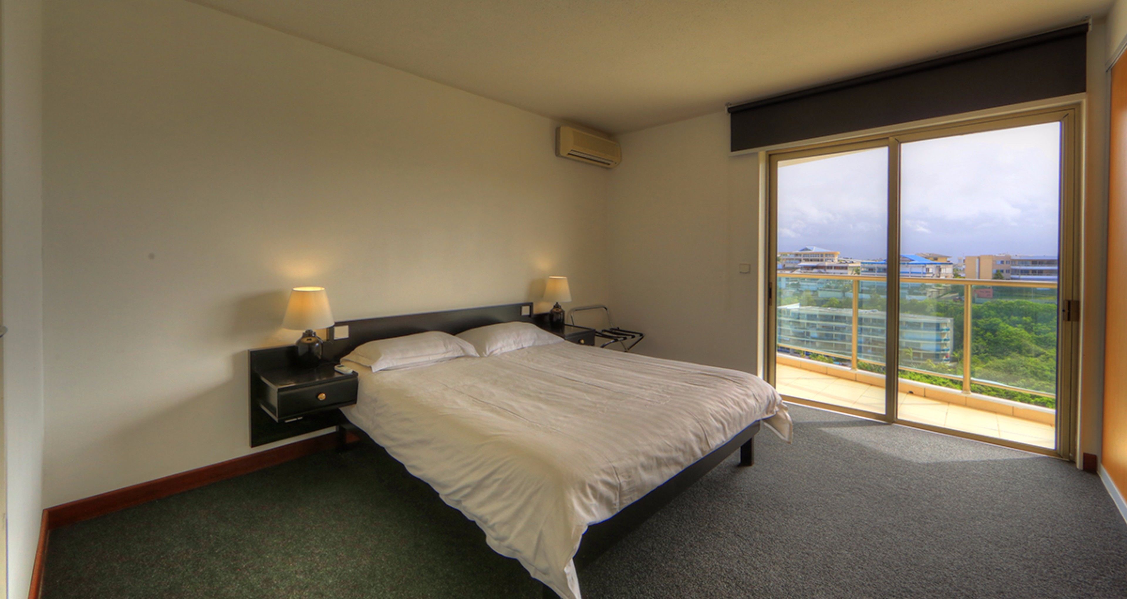 A hotel room with a bed, bedside tables, and a view of a cityscape through a large sliding glass door.