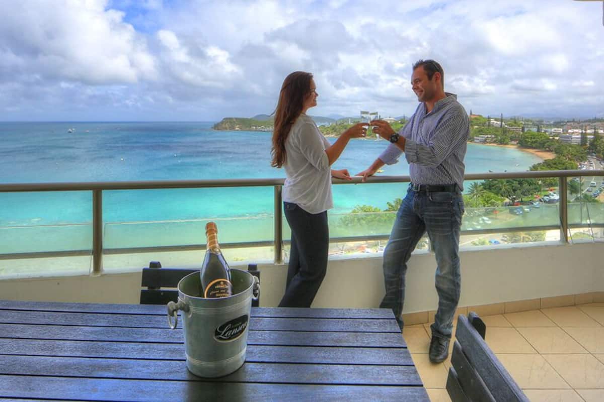 Ein Balkon mit Blick auf den Ozean, eine Champagnerflasche in einem Metallkübel und ein Tisch mit Bänken.