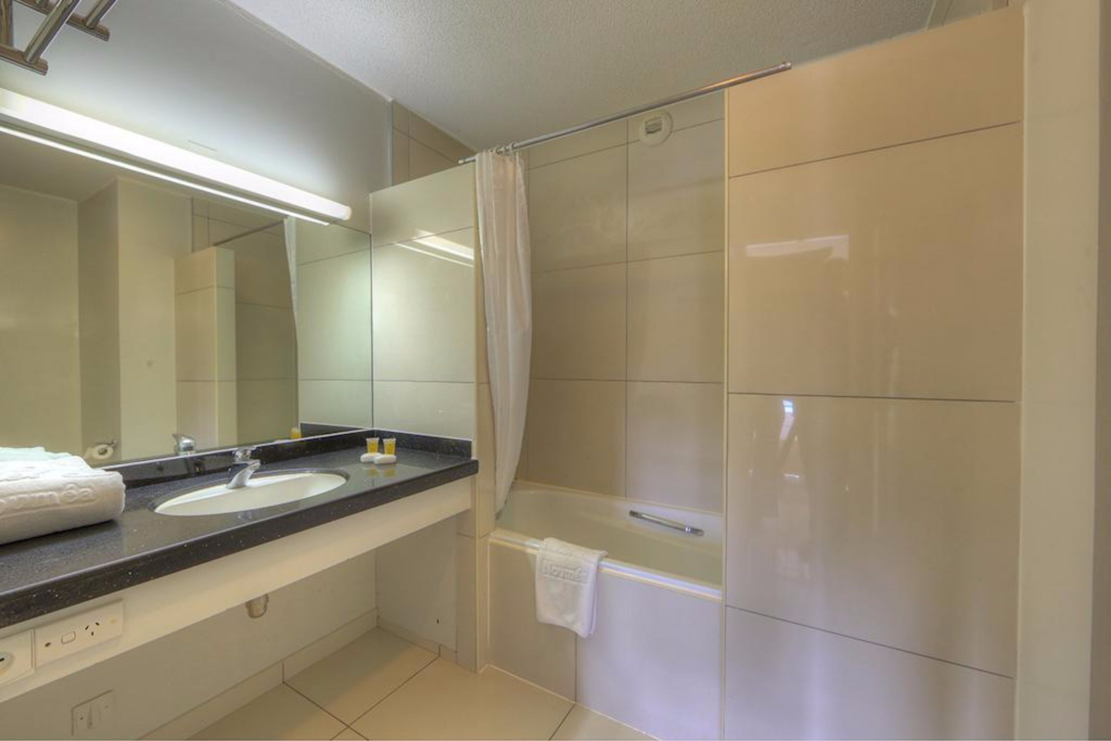 A modern bathroom with a large mirror, two sinks, a bathtub, and a shower curtain.