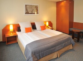 Habitación de hotel con cama doble, dos mesitas de noche con lámparas, un armario de madera y un taburete pequeño.
