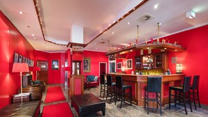 Uma área de bar com paredes vermelhas, balcão de madeira e vários bancos.