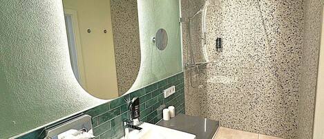 Un baño moderno con un espejo grande, un lavabo y una zona de ducha.