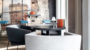 Un interior moderno con una mesa redonda, dos sillas, una lámpara y vistas a un edificio histórico a través de una ventana.