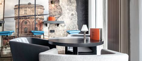 A modern interior with a round table, two chairs, a lamp, and a view of a historic building through a window.