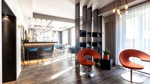 Un interior moderno con suelo de madera, una butaca curva color naranja, una zona de bar y un amplio ventanal con luz natural.