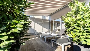 Una terraza de madera con mobiliario exterior y plantas en macetas.