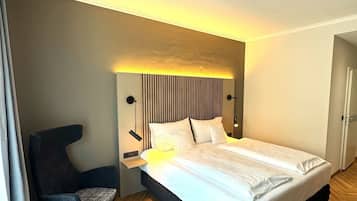 Ein modernes Hotelzimmer mit einem großen Bett, einem kleinen runden Tisch, einem Sessel und einem Kopfteil mit vertikalen Linien.