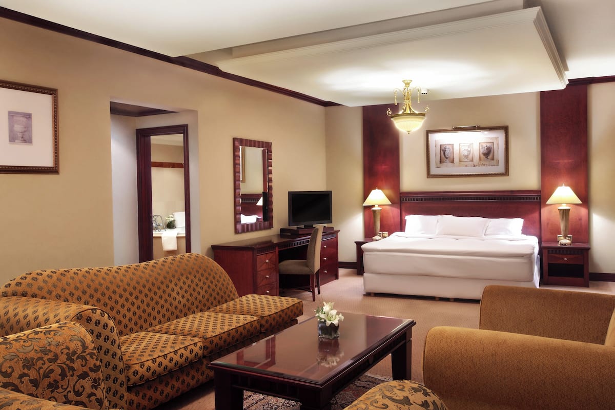 A hotel room with a sofa, a bed, a desk with a computer, and two bedside lamps.