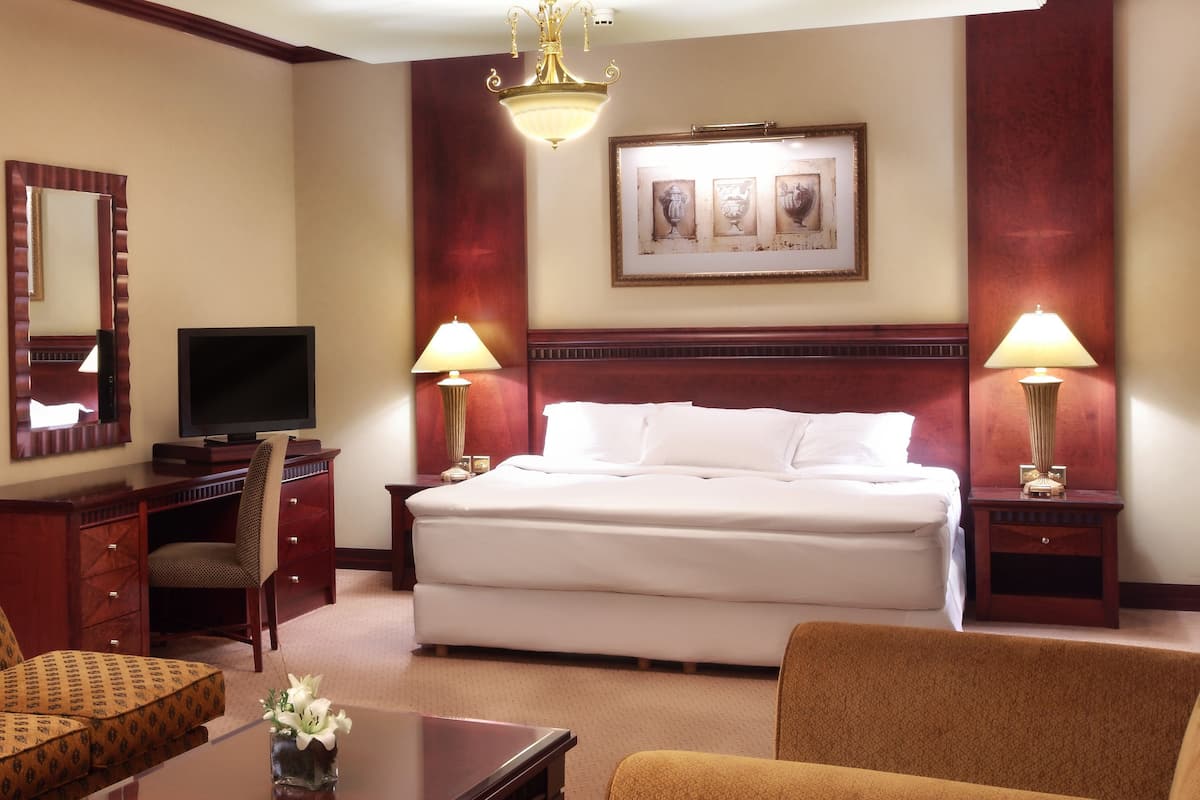 A hotel room with a large bed, two bedside lamps, a television, a desk with a chair, and a decorative mirror.