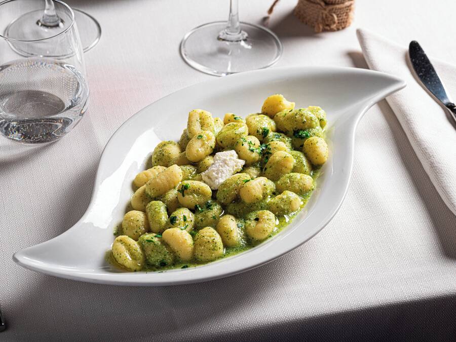 A white plate with gnocchi and a dollop of cream, accompanied by a knife and a glass of water on a table.