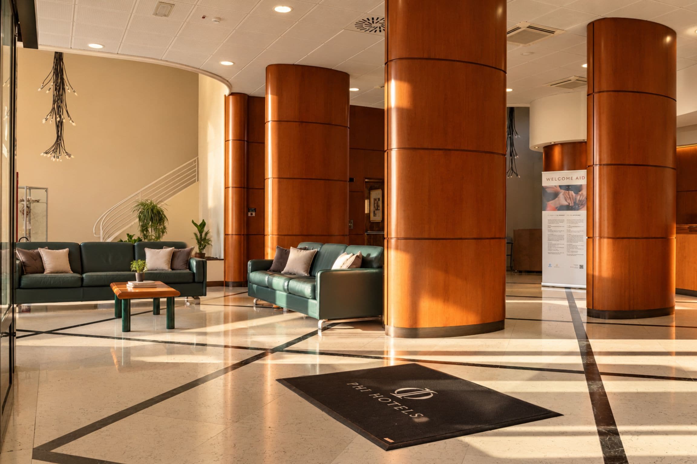 Un hall d’hôtel comprenant un comptoir d’accueil, deux canapés, une table basse et un tapis noir orné d’un logo.