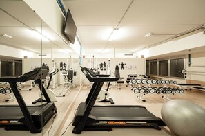 Une salle de sport équipée de tapis de course, d’appareils de musculation et de poids libres.