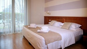 A hotel room with a large bed, a wooden headboard, a bedside lamp, and a view through a window with sheer curtains. - Phi Hotel Emilia (Ozzano dell'Emilia)