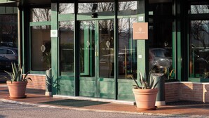 A hotel entrance with green doors, a sign indicating 'PHI HOTELS', and potted plants on the sidewalk. - Phi Hotel Emilia (Ozzano dell'Emilia)