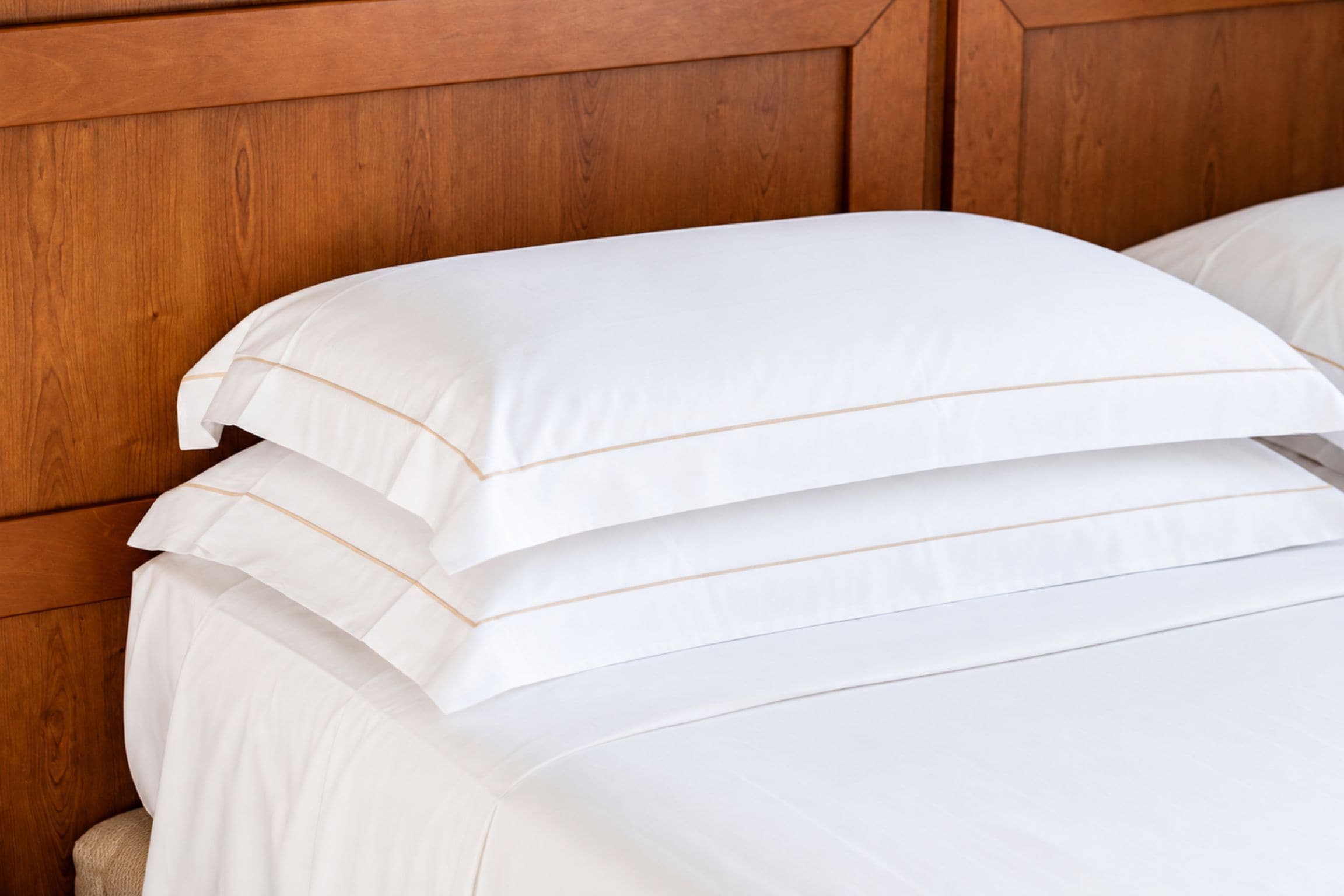 Almohadas blancas apiladas con un detalle de diseño en un cabecero de madera.