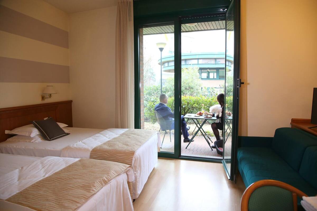 Ein Hotelzimmer mit zwei Betten, einem Schlafsofa und einer Glastür zu einem Sitzbereich im Freien.