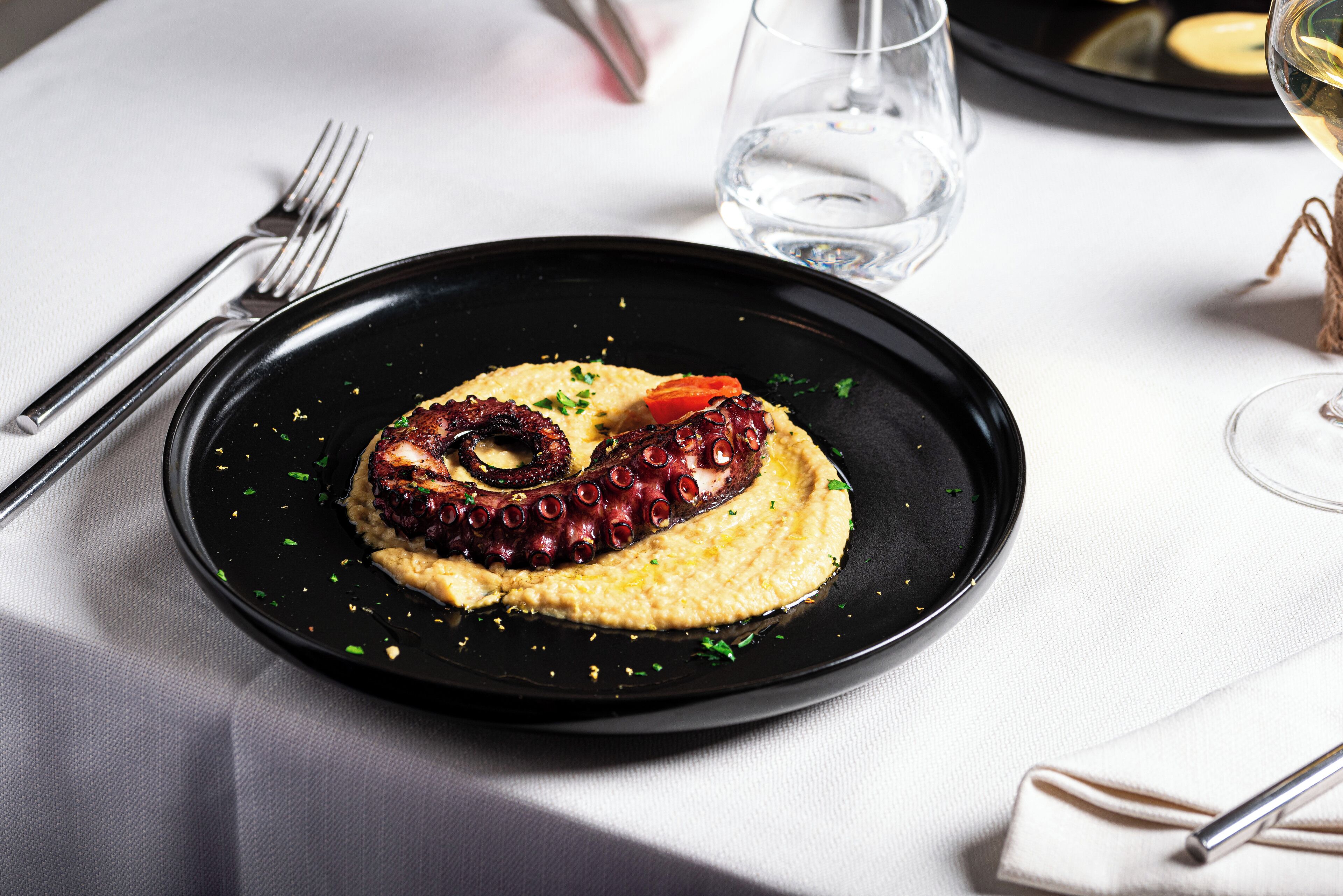 A black plate with octopus and a tomato on a white tablecloth.
