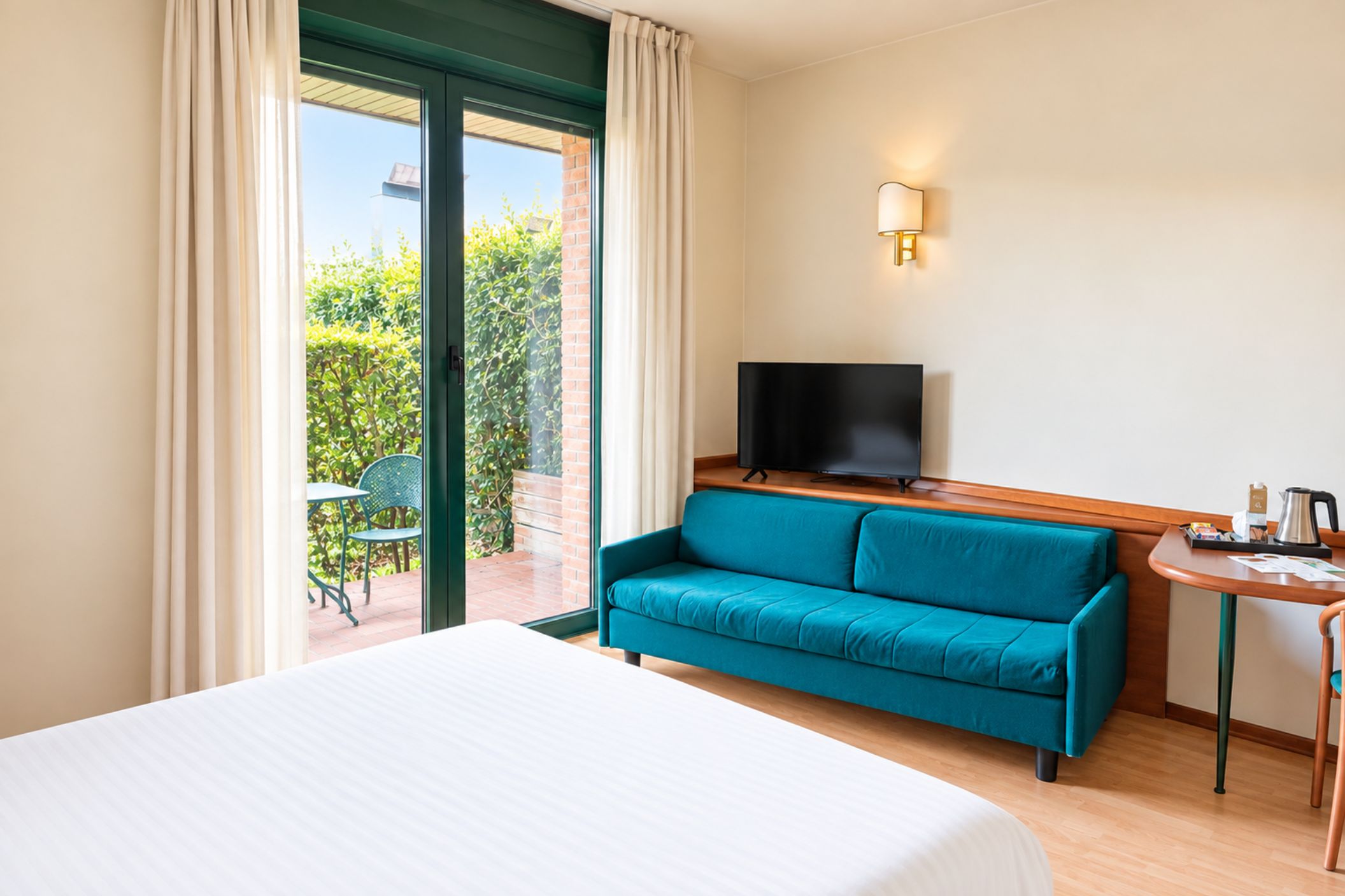 Ein Hotelzimmer mit einem Bett, einem türkisfarbenen Sofa, einem Fernseher und einem kleinen Tisch mit einem Wasserkocher.