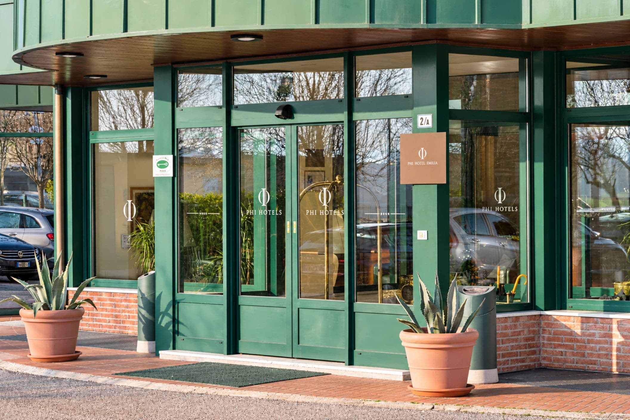 A hotel entrance with green doors, a sign for room 2/A, and potted plants.