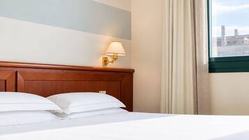 Habitación de hotel con cabecera de madera, cama con ropa blanca, lámpara de pared y ventana con cortinas.