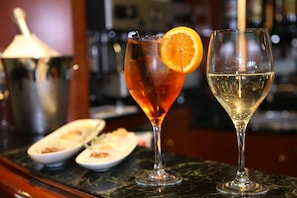 Two glasses of beverages on a marble bar counter, one with a slice of orange.