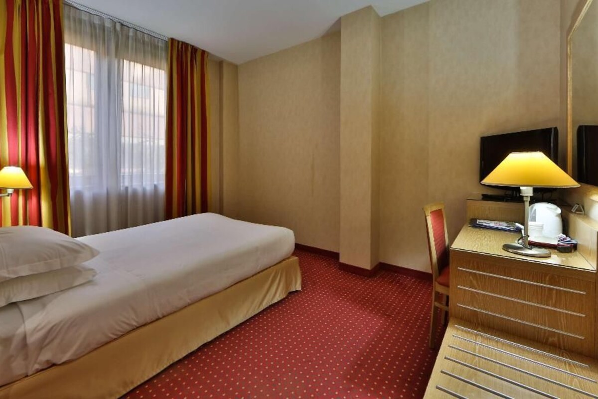 A hotel room with a bed, a desk, a chair, a television, and a lamp.