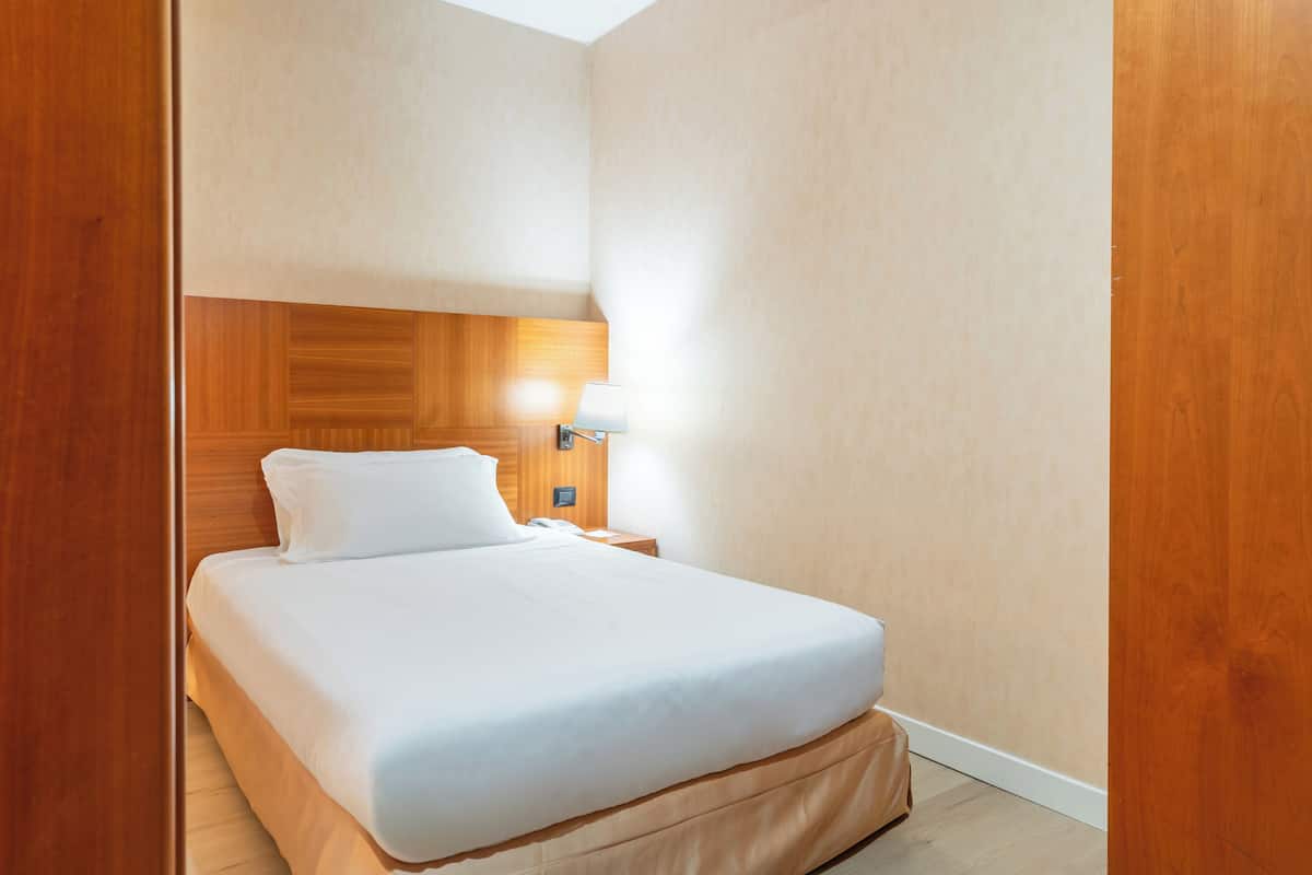 A hotel room with a bed, a nightstand, a lamp, and a wooden headboard.