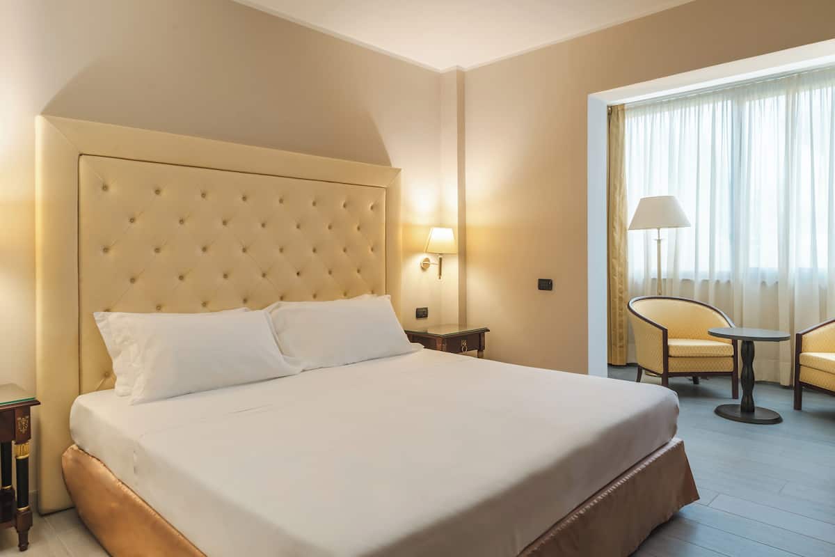 A hotel room with a large bed, a nightstand, a lamp, a chair, and a table.