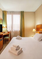 A hotel room with a bed, a desk, a chair, a television, and a lamp.