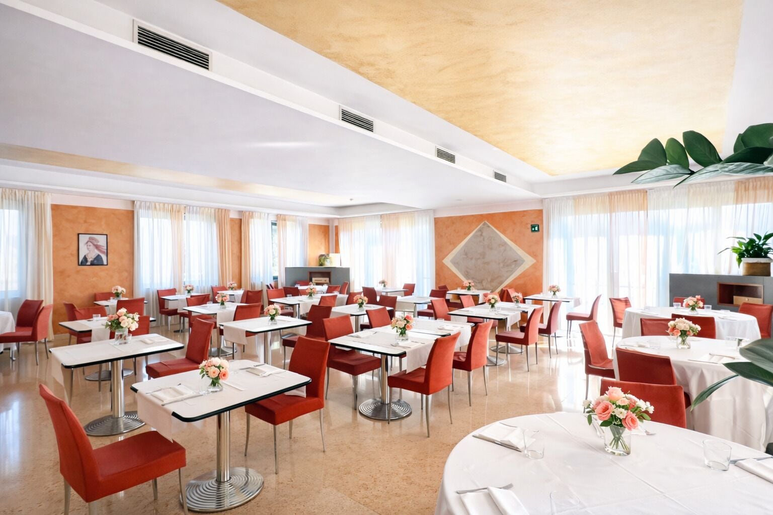 A hotel dining area with multiple tables and chairs, a fireplace, and large windows.