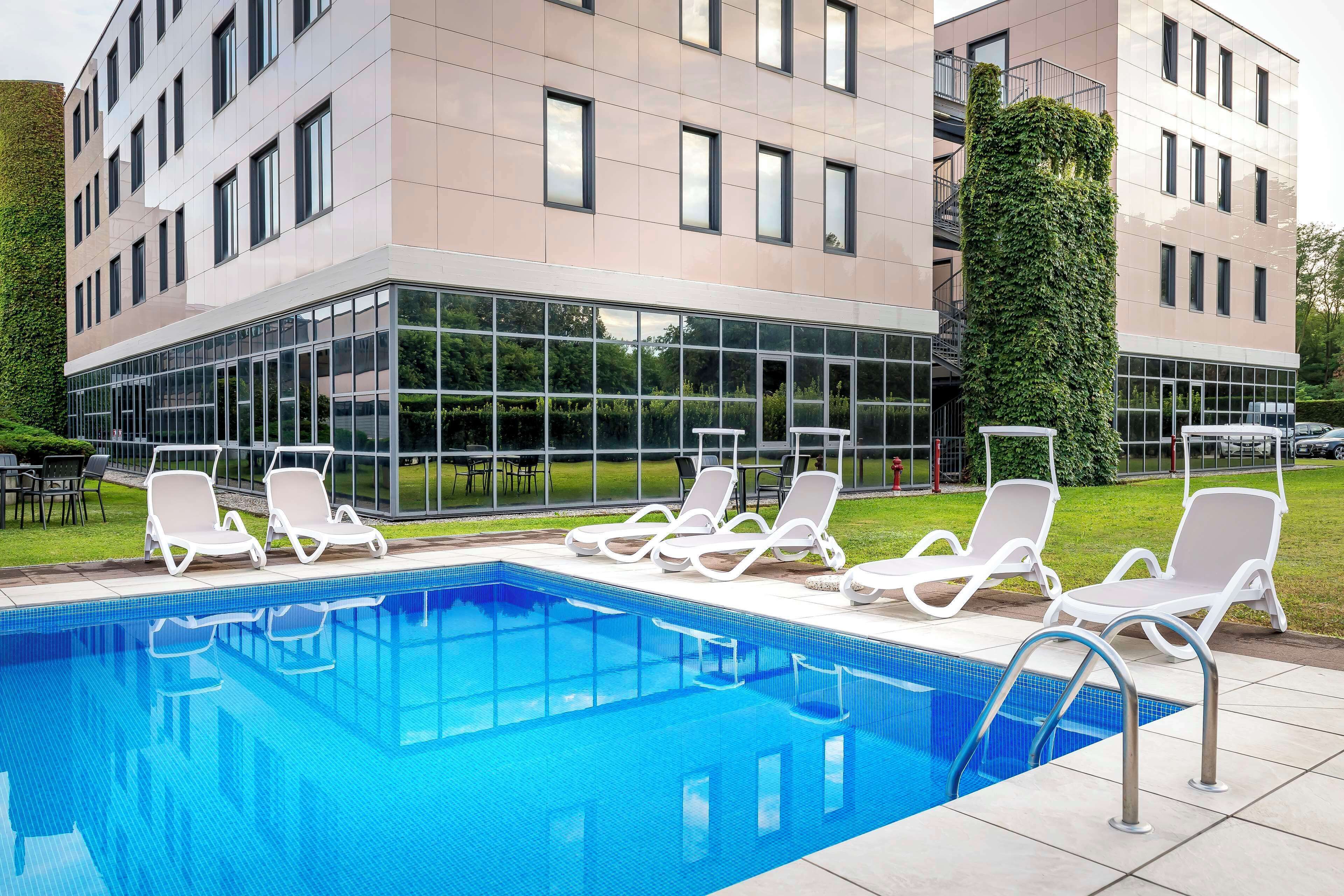 Ein modernes Gebäude mit Schwimmbad, weißen Liegestühlen und einer Glasfassade.
