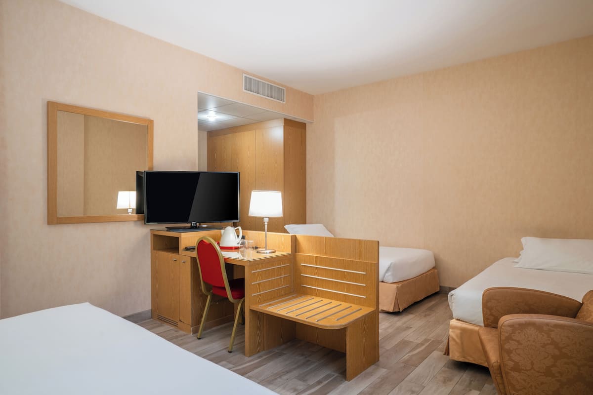 A hotel room with a bed, a desk with a computer, a chair, a television, and a mirror.