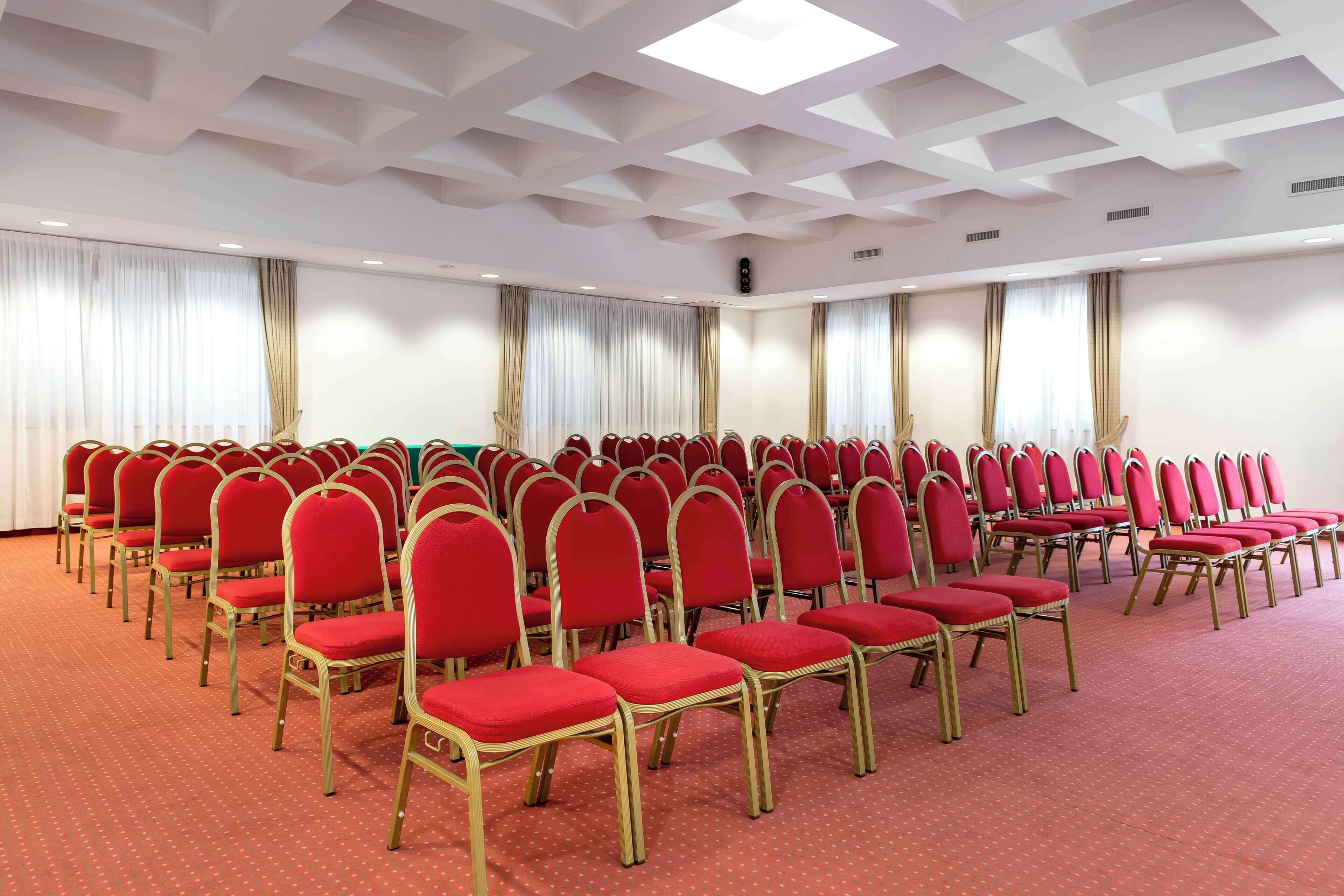 A conference room with rows of red chairs and a patterned carpet.