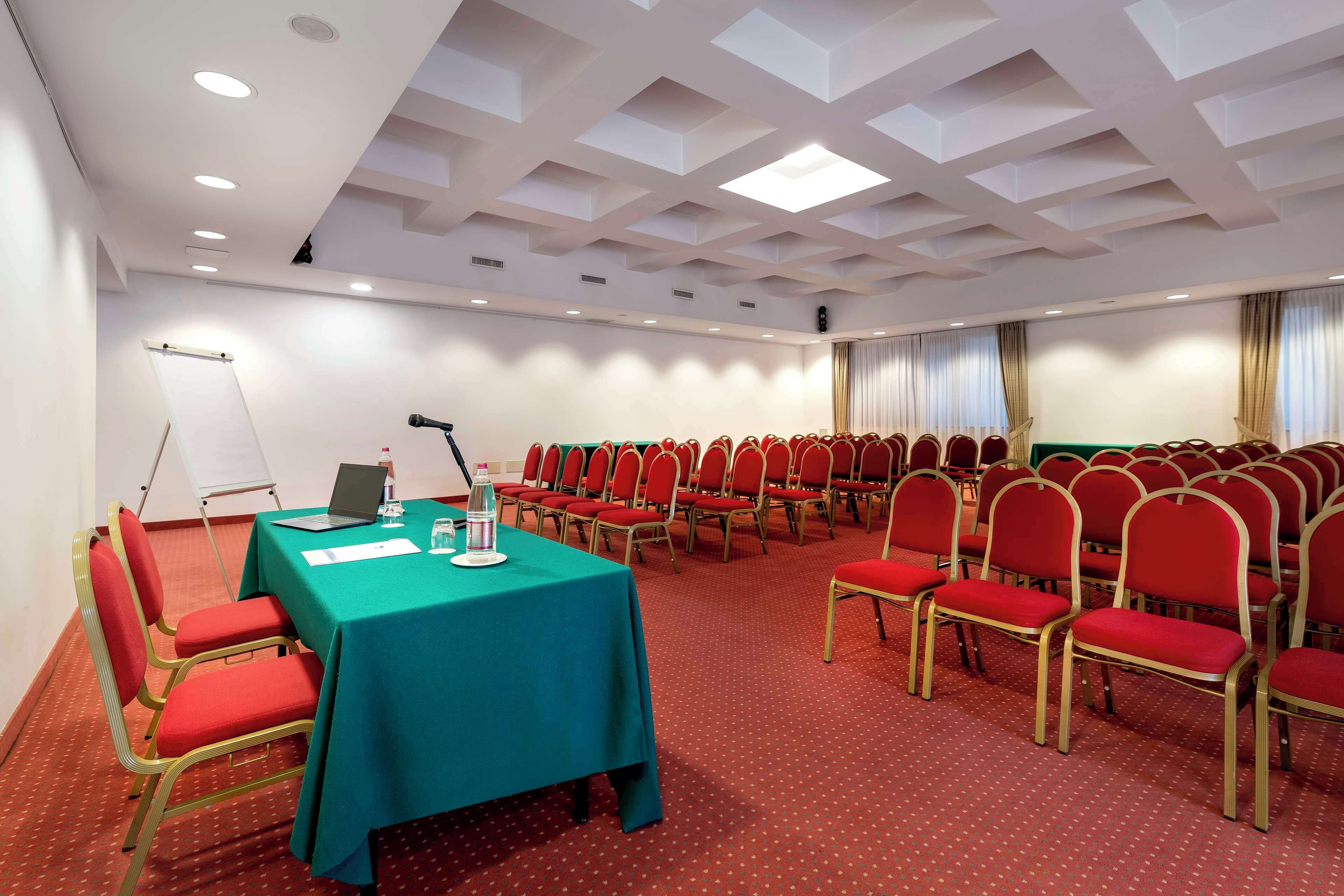 Un salón de conferencias con una mesa verde, sillas rojas y una pizarra.