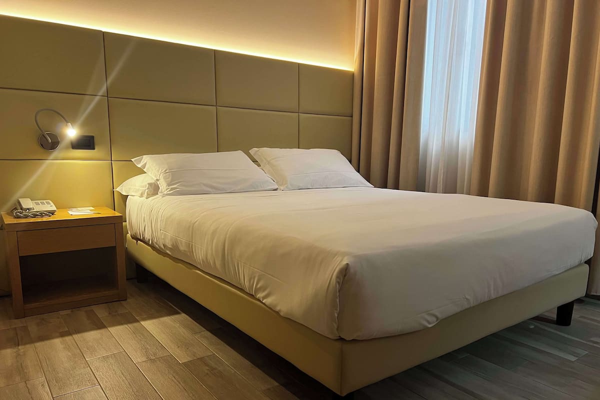 A neatly made bed with white linens, a bedside table with a phone, and a wall-mounted light fixture.