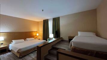 Quarto de hotel com duas camas, uma escrivaninha, uma cadeira, uma televisão e uma janela com cortinas.